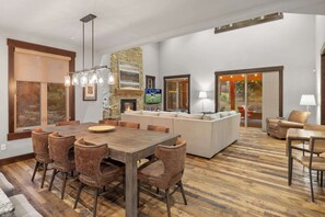 A spacious living area with a wooden dining table, comfortable seating, a stone accent wall, and a television. - Lux 5BR, Fairway View, GameRm, Firepit, ChefsKitch (Cle Elum)