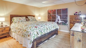 Un dormitorio con cama de madera, mesita de noche, cómoda y una ventana grande con vista a árboles.