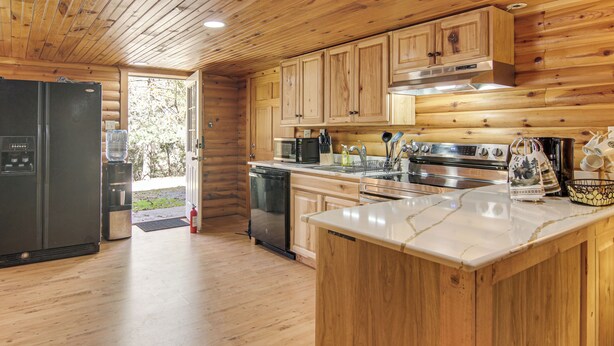 Cocina de cabaña de madera con refrigerador, lavavajillas, microondas, estufa y armarios de madera.