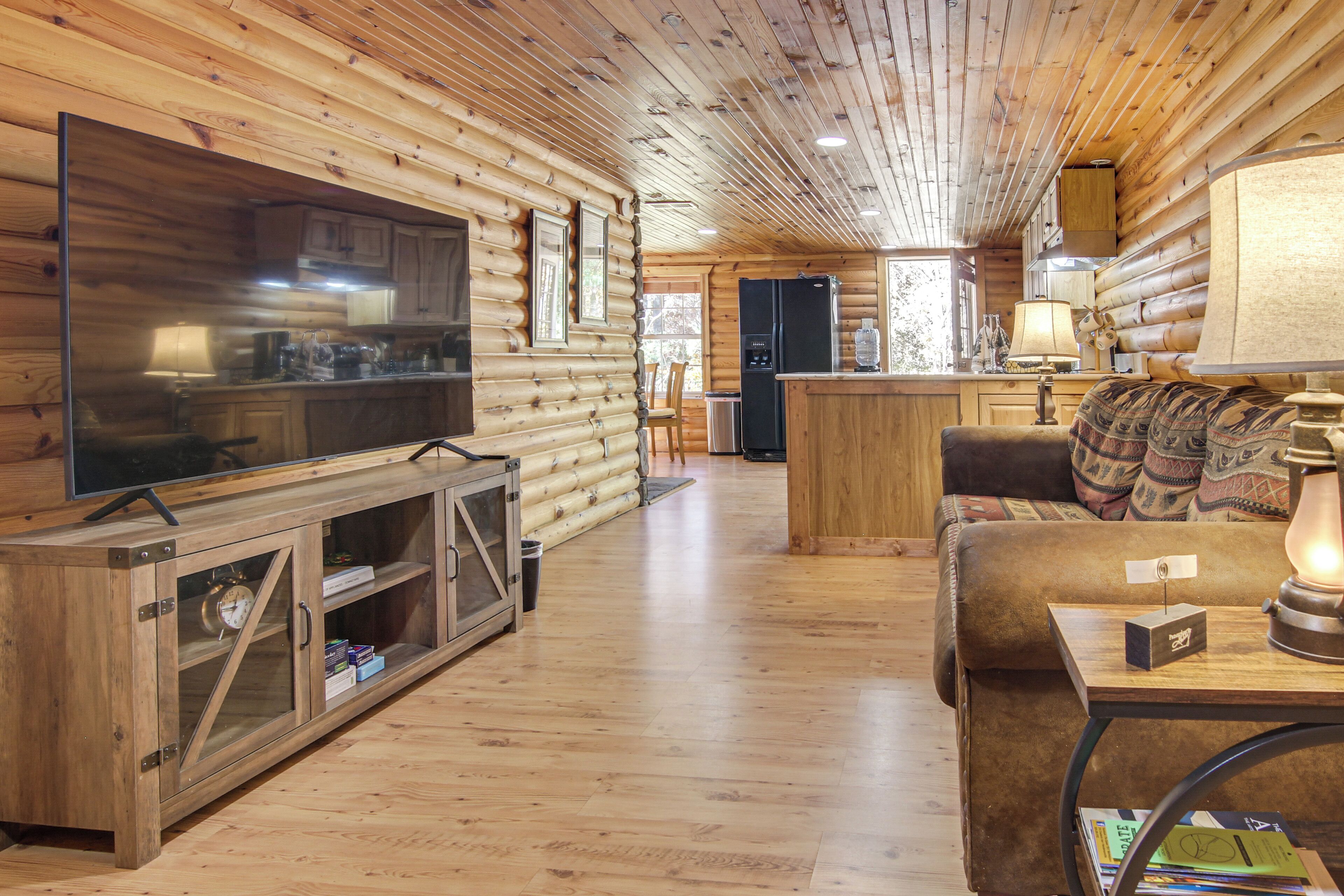 A log cabin interior with a television, wooden cabinets, a sofa, and a kitchen area.