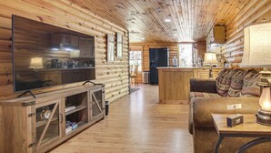 Interior de una cabaña de madera con televisión, armarios de madera, un sofá y una zona de cocina.