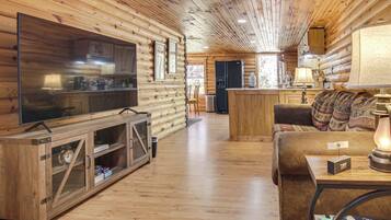A log cabin interior with a television, wooden cabinets, a sofa, and a kitchen area.