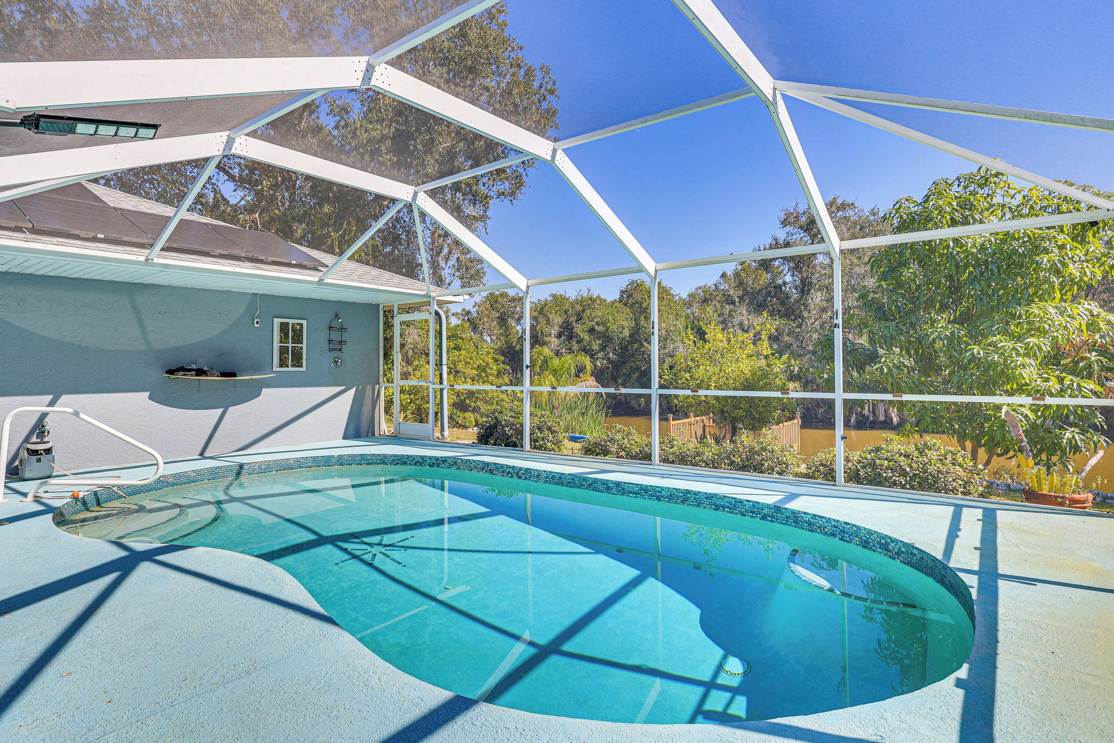 Una piscina con un recinto in vetro, circondata da alberi e un cielo sereno.