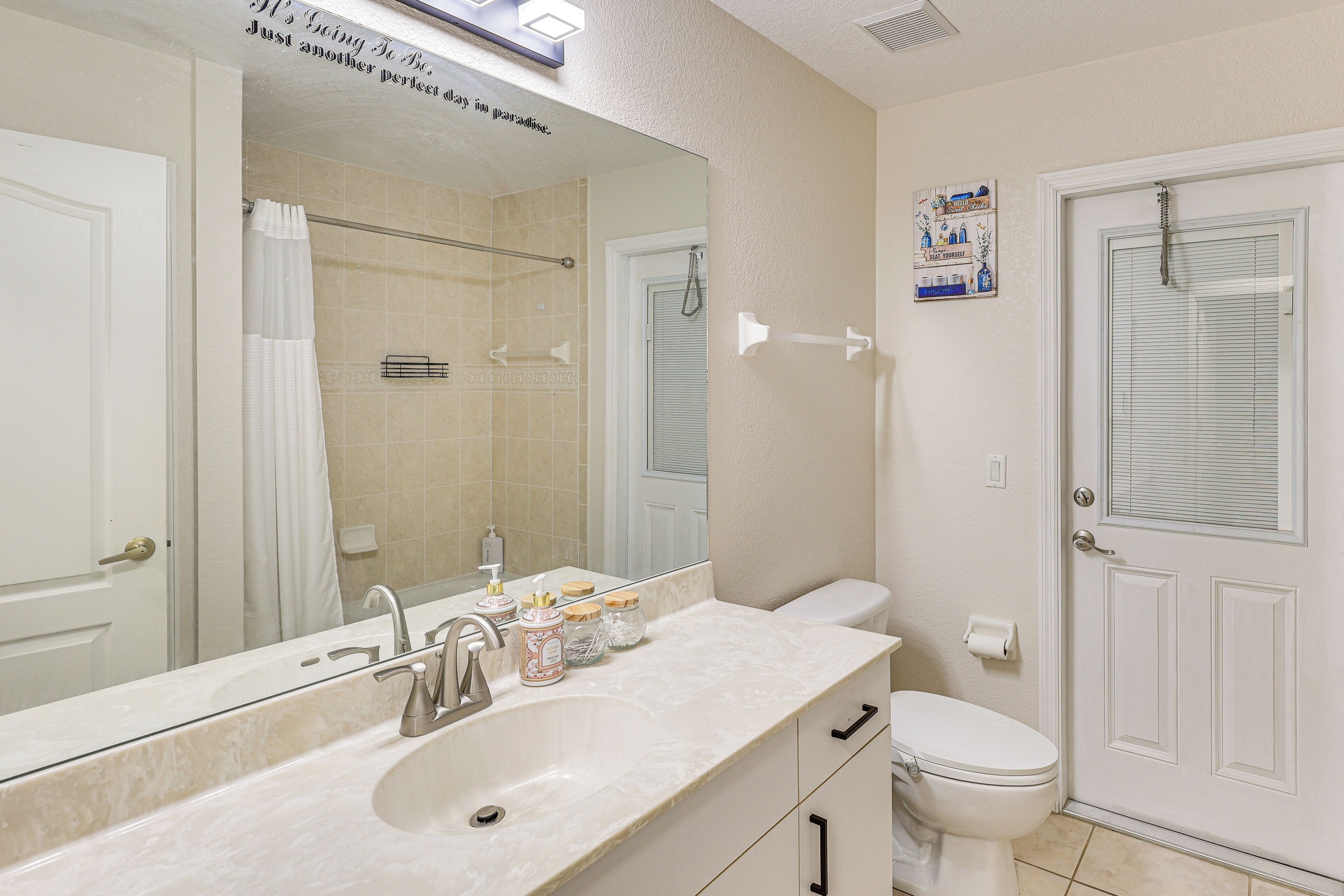 Une salle de bain comprenant un grand miroir, un lavabo avec des articles de toilette, des toilettes et un espace douche.