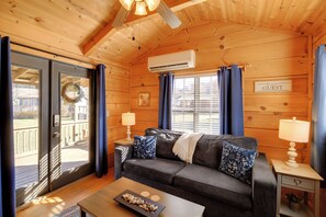 A cozy log cabin room with a dark gray sofa, two matching lamps, a wooden ceiling, and a sign that reads "be our guest". - Hike the AT! Creekside Cabin in Trail Town USA (Damascus)