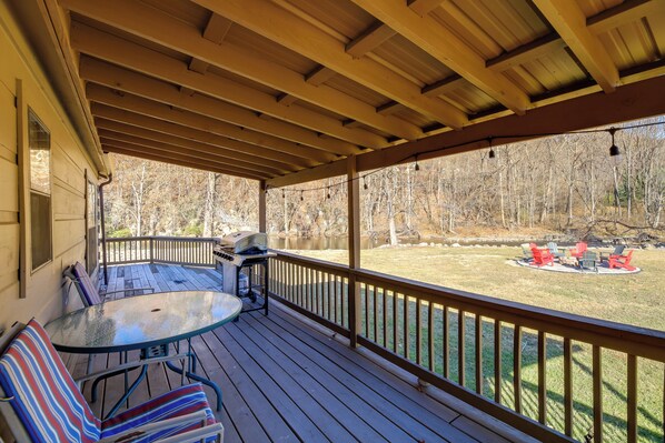 Une terrasse couverte avec une table et des chaises, un barbecue et une vue sur une cour arrière agrémentée d’un foyer extérieur.