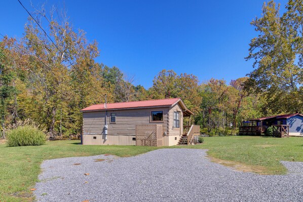 A small wooden cabin with a red roof, a gravel driveway, and a wooden deck. - Hike the AT! Creekside Cabin in Trail Town USA (Damascus)