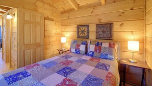 Une chambre dans une cabane en bois, avec un grand lit, deux lampes fixées au mur et une porte.