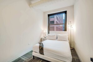 A hotel room with a large bed, a nightstand, a lamp, and a view of buildings through a window. - Downtown Chicago Stay with Free In & Out Parking 3 (Chicago)