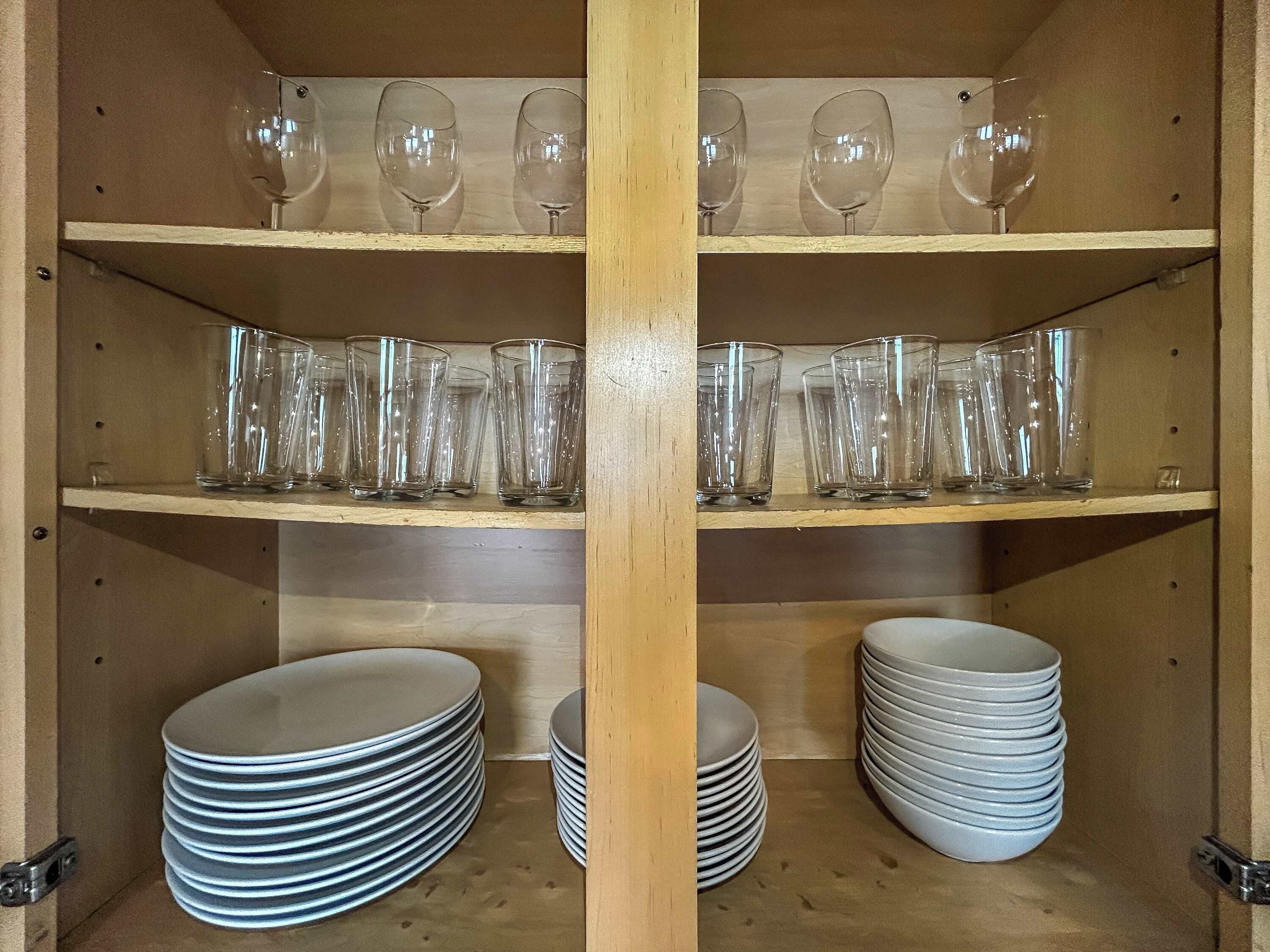A wooden cabinet with shelves holding wine glasses and stacked plates.