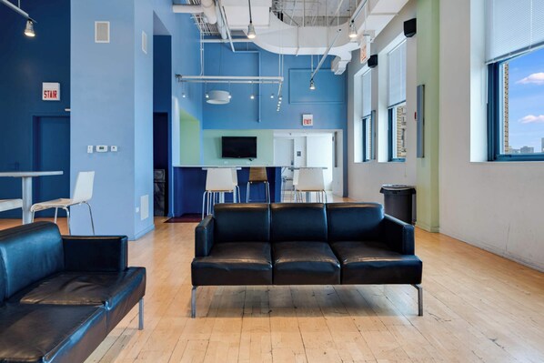 A modern lounge area with a black leather sofa, a small table, and chairs. There is a television mounted on the wall and an exit sign above the door.