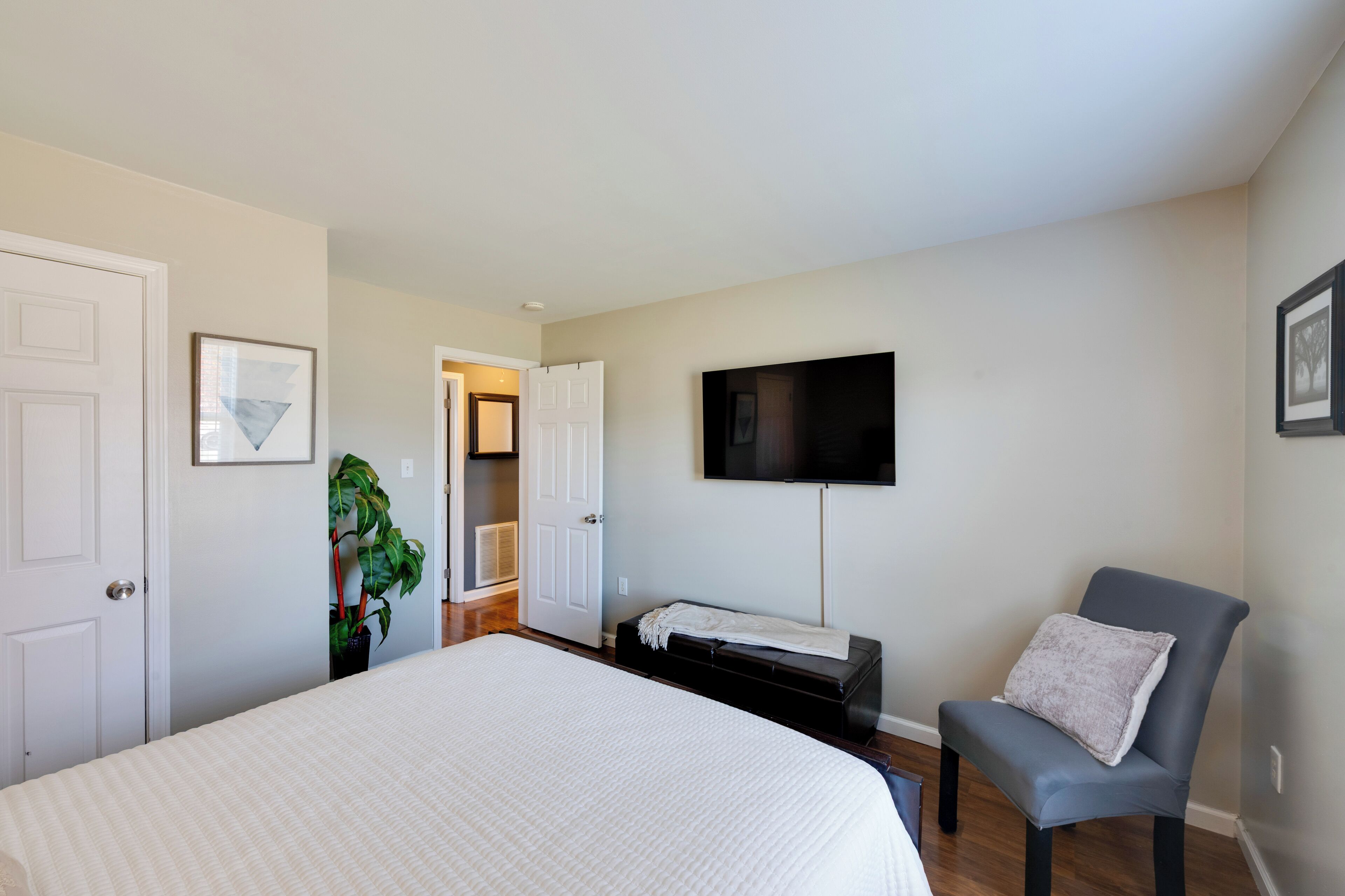 A bedroom with a bed, a chair, a TV, and a door leading to another room.