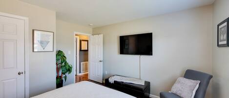 A bedroom with a bed, a chair, a TV, and a door leading to another room.