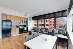 A modern apartment with a kitchen, dining area, and living room. It features large windows, a black refrigerator, and a grey sofa set. - Downtown Chicago Stay with Free In & Out Parking 5 (Chicago)