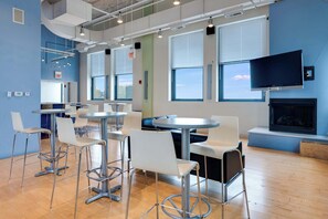 Un intérieur moderne avec de nombreuses tables et chaises, de grandes fenêtres et un téléviseur à écran plat fixé au mur.