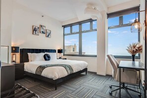 A hotel room with a large bed, a desk, and a view of the city through large windows. - Downtown Chicago Stay with Free In & Out Parking 6 (Chicago)