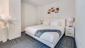 Habitación de hotel con una cama grande, dos mesitas de noche, un jarrón con flores blancas y arte abstracto en la pared.