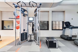 Un gimnasio con barra de dominadas, torre de pesas, cinta de correr y una pantalla digital.