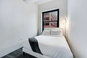 A modern hotel room with a large bed, a window with blinds, and a bedside lamp. - Downtown Chicago Stay with Free In & Out Parking 4 (Chicago)