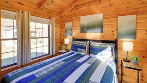 Ein Schlafzimmer einer Holzhütte mit einem großen Bett, zwei Nachttischen mit Lampen und einem Fenster mit Vorhängen.