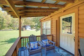 A wooden porch with two Adirondack chairs and a bench, a door with a window, and a view of a house and trees in the background. - Pet-Friendly Damascus Cabin w/ Deck & Mtn Views! (Damascus)