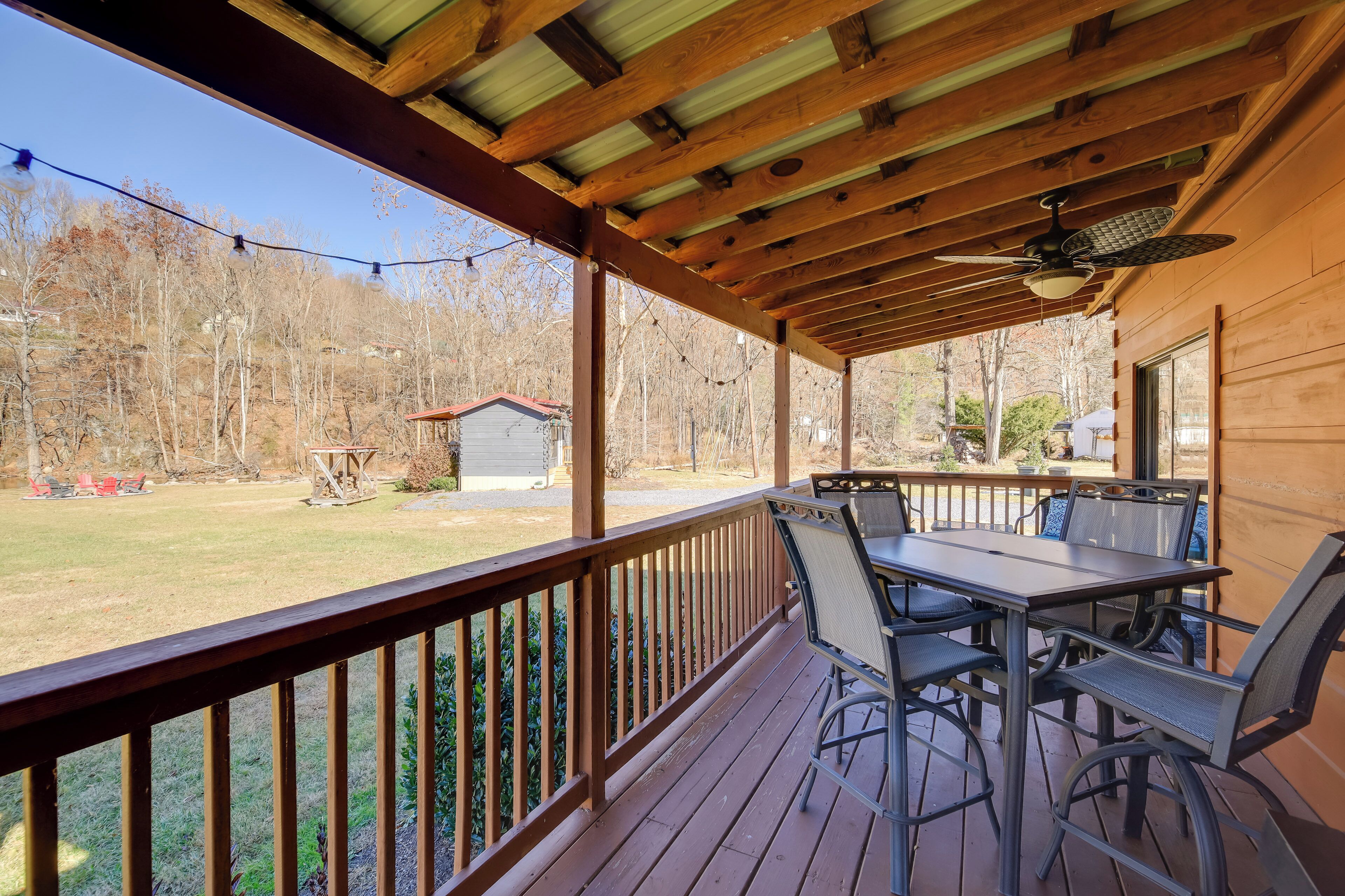 A covered outdoor patio with a table and chairs, a ceiling fan, and a view of a yard with trees and a shed.