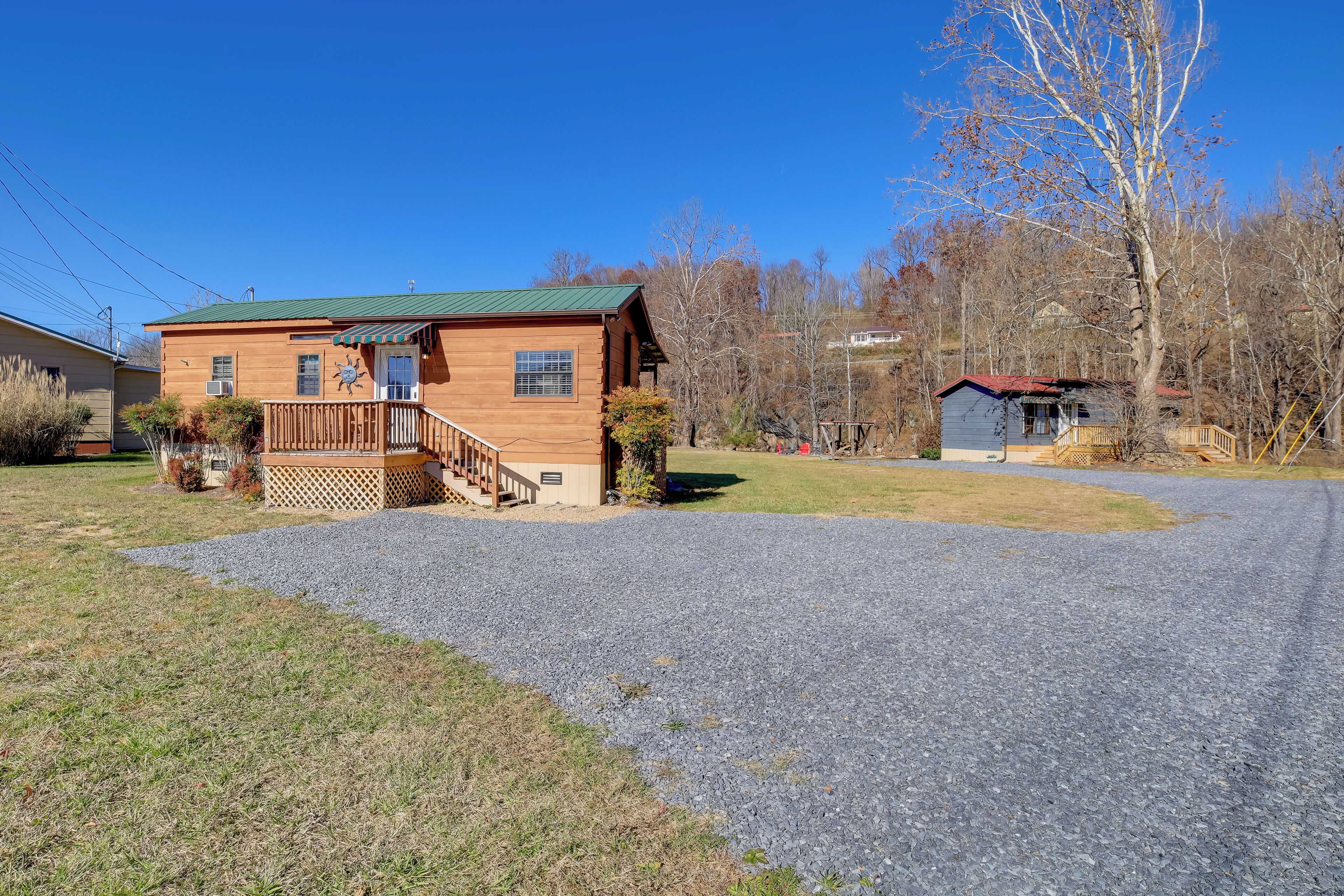 A wooden cabin with a green roof, a wooden deck, and a gravel driveway.