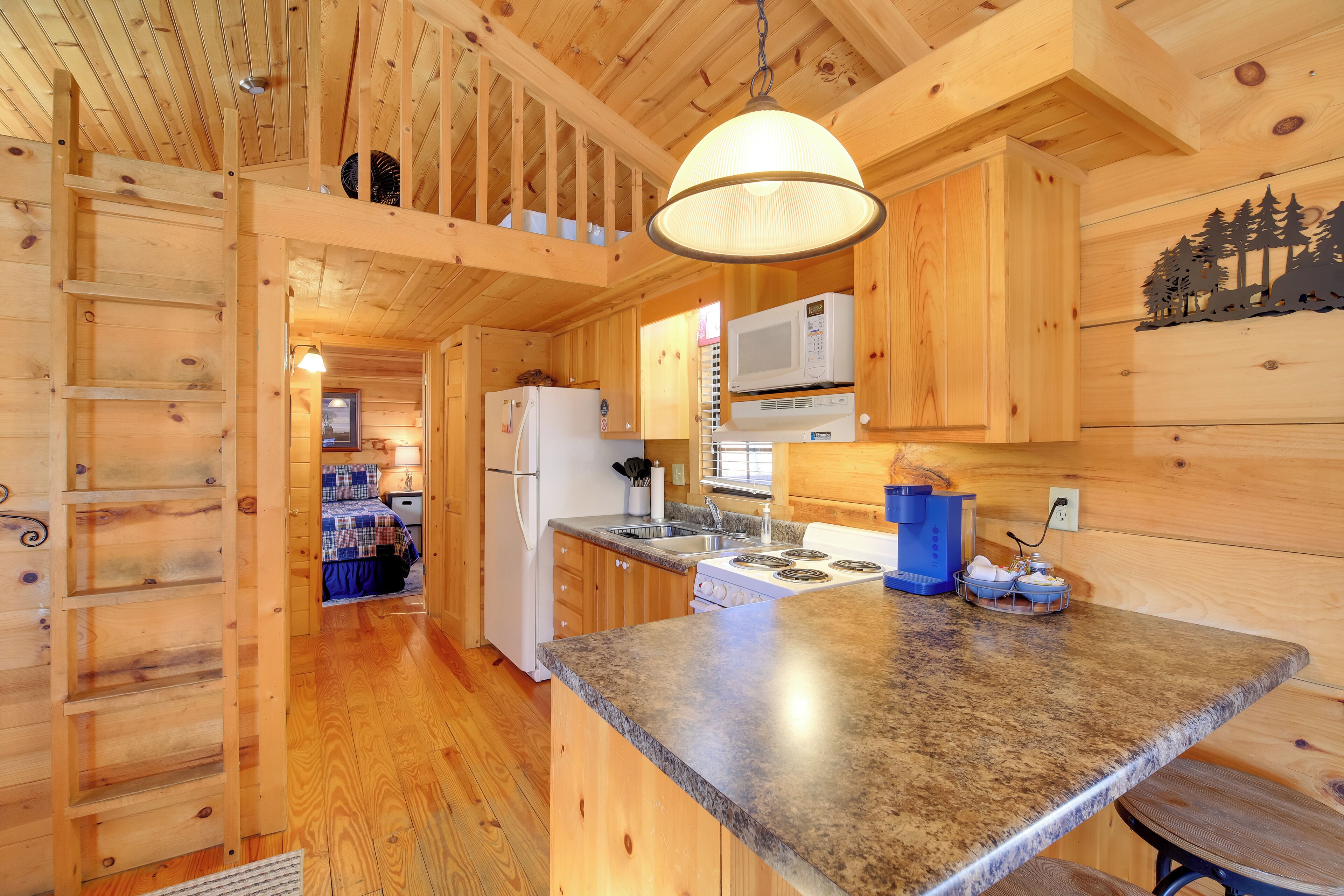 A wooden cabin interior with a kitchen area, including a stove, microwave, and wooden cabinets.