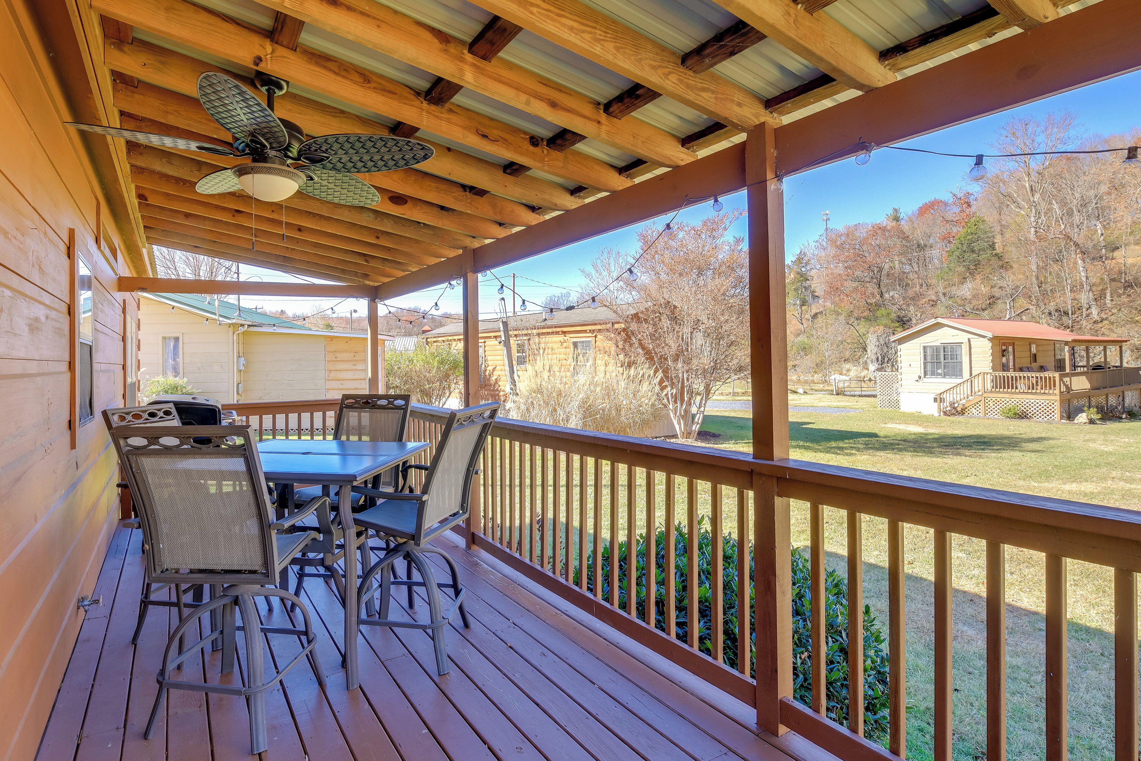 Une terrasse en bois avec une table et des chaises, un ventilateur de plafond et une vue sur un quartier résidentiel.