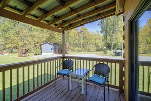 A wooden deck with two wicker chairs and a small table, overlooking a grassy area with trees and a small building. - Bike, Hike, Ride & Fish from Cozy Creekside Cabin (Damascus)