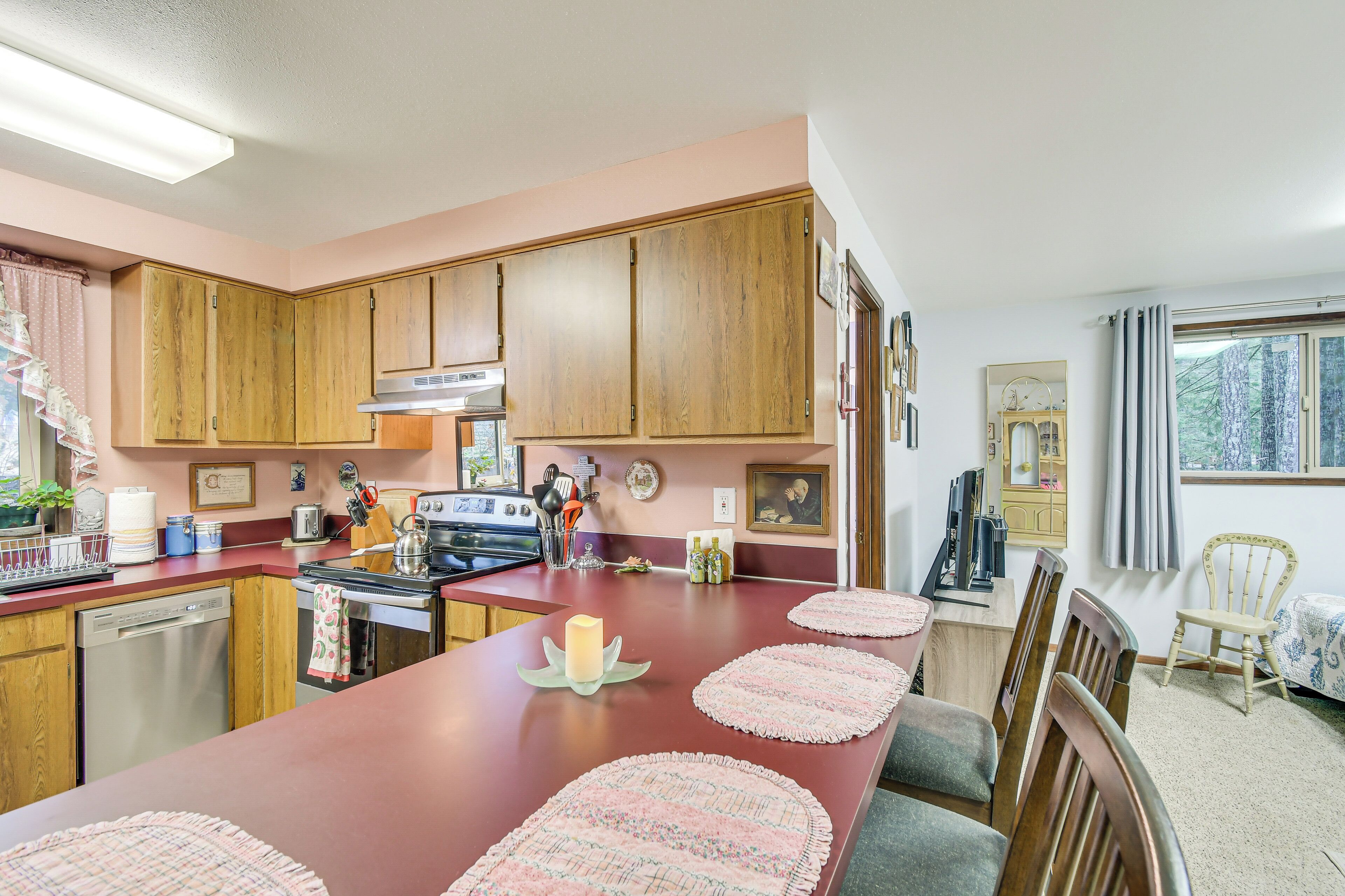 Een keuken met houten kastjes, een centraal eiland met roze placemats, een vaatwasser, een oven en een kookplaat.
