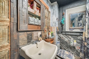 A bathroom with a sink, shelves with toiletries, and a mirror.