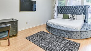 Une chambre à coucher avec un lit doté d’une tête de lit capitonnée, un bureau avec une chaise et une grande fenêtre avec des rideaux.