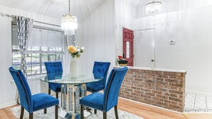 Un coin repas avec une table en verre entourée de chaises bleues, un tapis à poils longs blanc et un mur décoratif en briques.