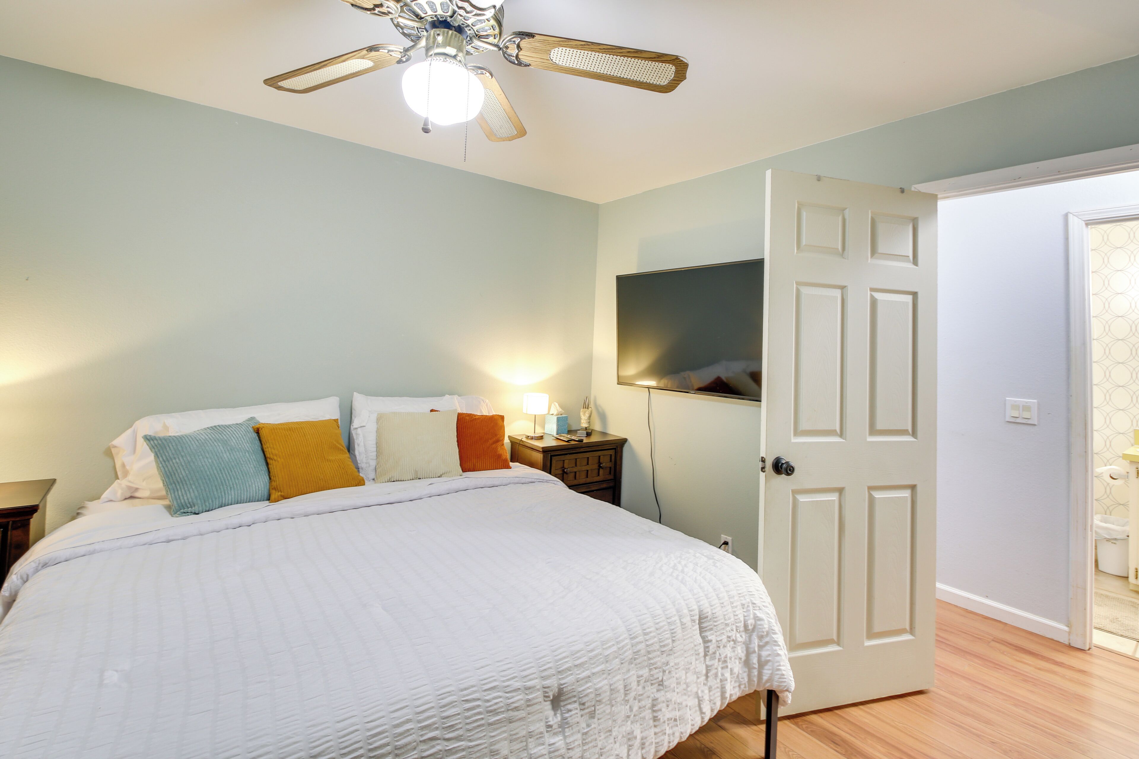 A bedroom with a bed, a nightstand, a ceiling fan, and a door leading to another room.