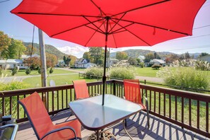 A deck with a table and chairs, an umbrella, and a view of houses and hills in the background. - Trail Town USA! 2BD Cabin on Laurel Creek w/ Deck (Damascus)