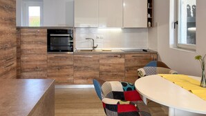 A modern kitchen with wooden cabinets, a built-in oven, and a sink. There is a dining area with a white table and colorful chairs. - Awesome home in Liznjan (Liznjan)