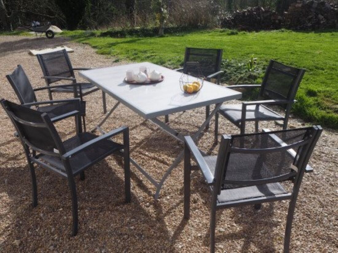 A white table with four black chairs, a tray with a bowl of fruit, and a white pitcher.