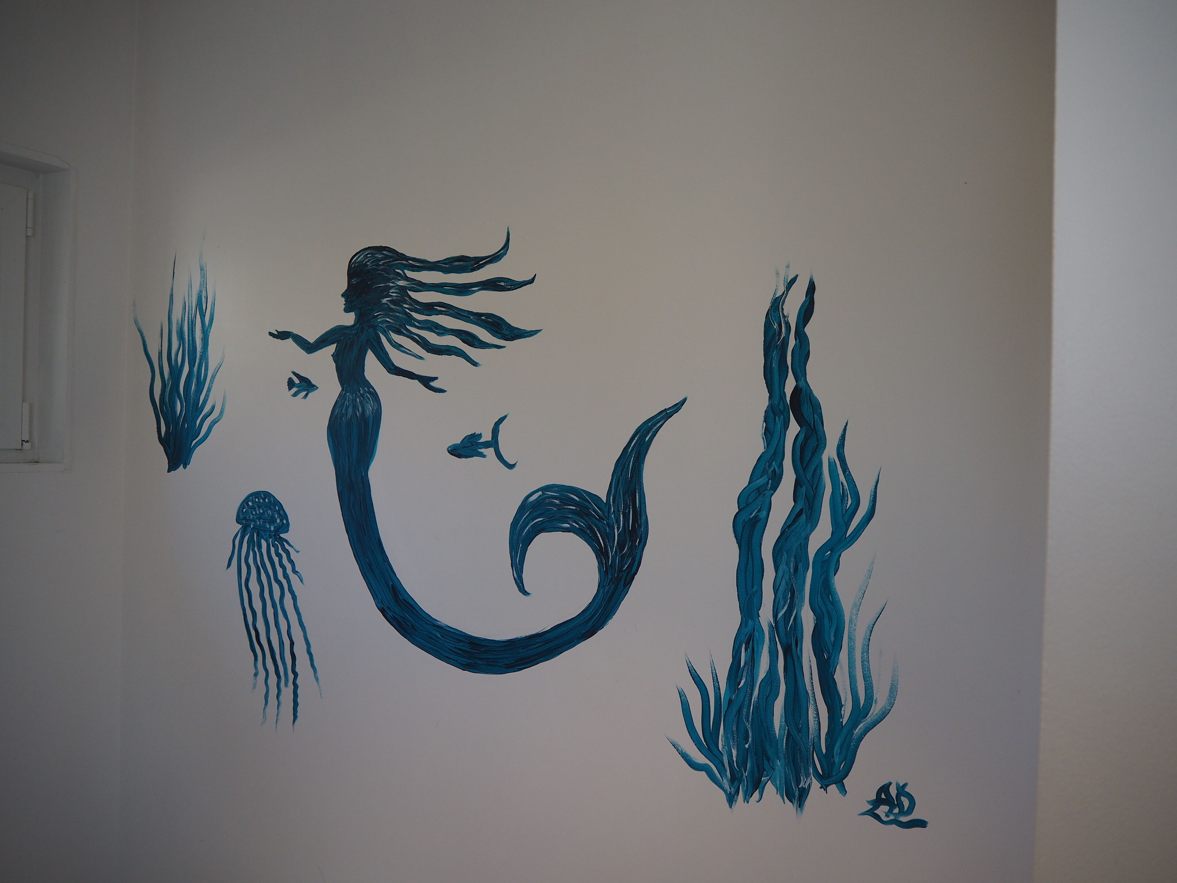 Una pared con una ilustración de sirena y decoración temática marina.