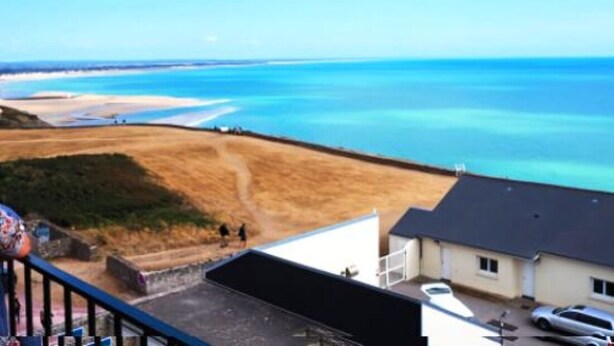 A coastal view with a clear sky, a sandy beach, and a few buildings in the foreground.