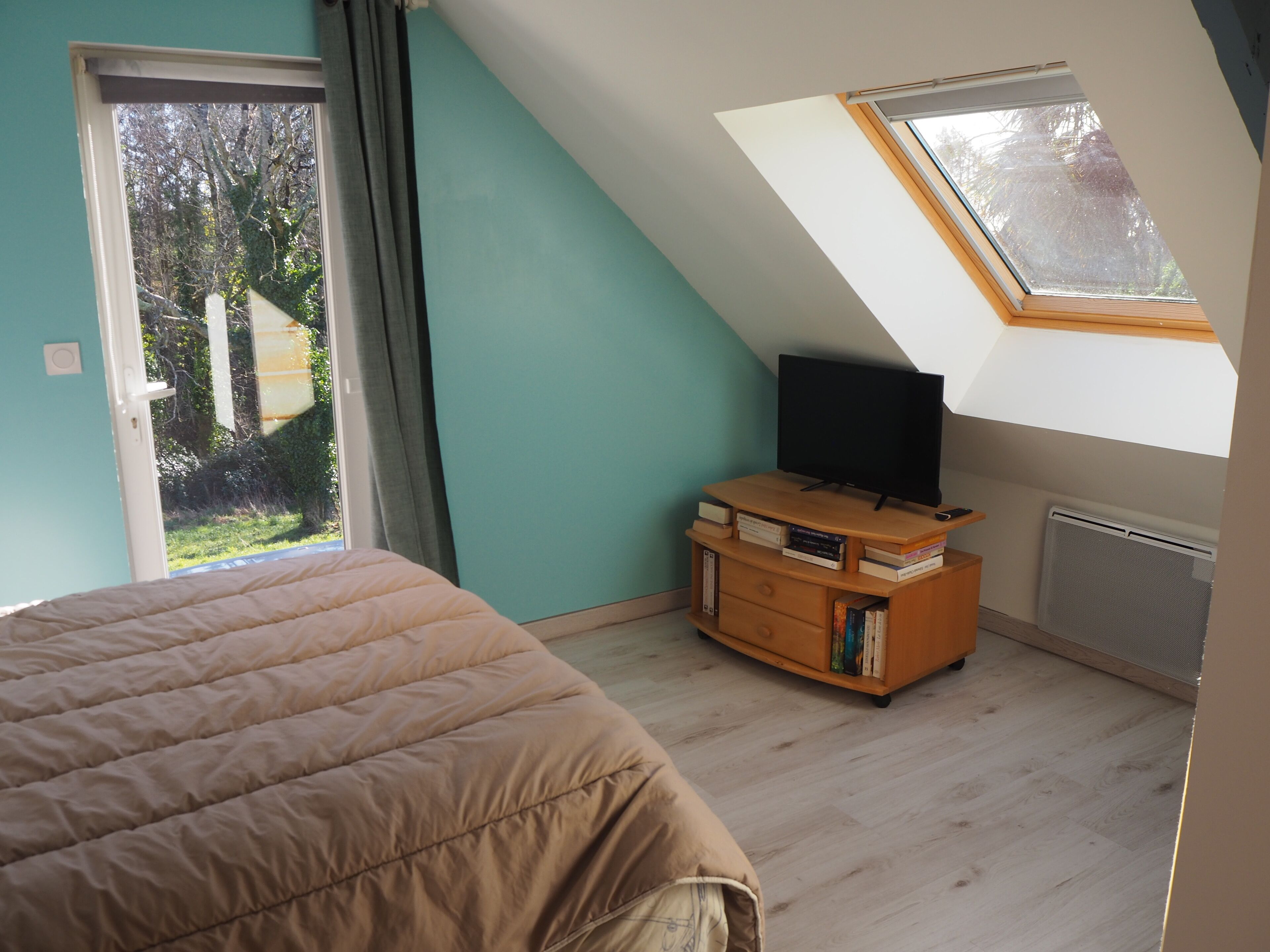 A bedroom with a bed, a TV on a wooden stand, a window, and a skylight.