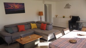 A living room with a grey sofa, a wooden coffee table, and a dining table with a checkered tablecloth.