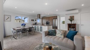 A modern kitchen with a central island, a dining area with a table and chairs, and a living area with a sofa and a coffee table. - Endless Summer Retreat - Mt Maunganui (Mount Maunganui)