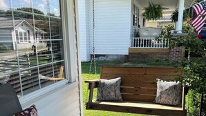 Een overdekte veranda met een houten schommel, een bank en een stoel.