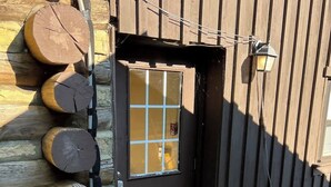 A wooden cabin with a black door, a window with a grid pattern, and logs stacked against the wall. - The Barn at Wendover - 4 BR 2 BA (Wendover)