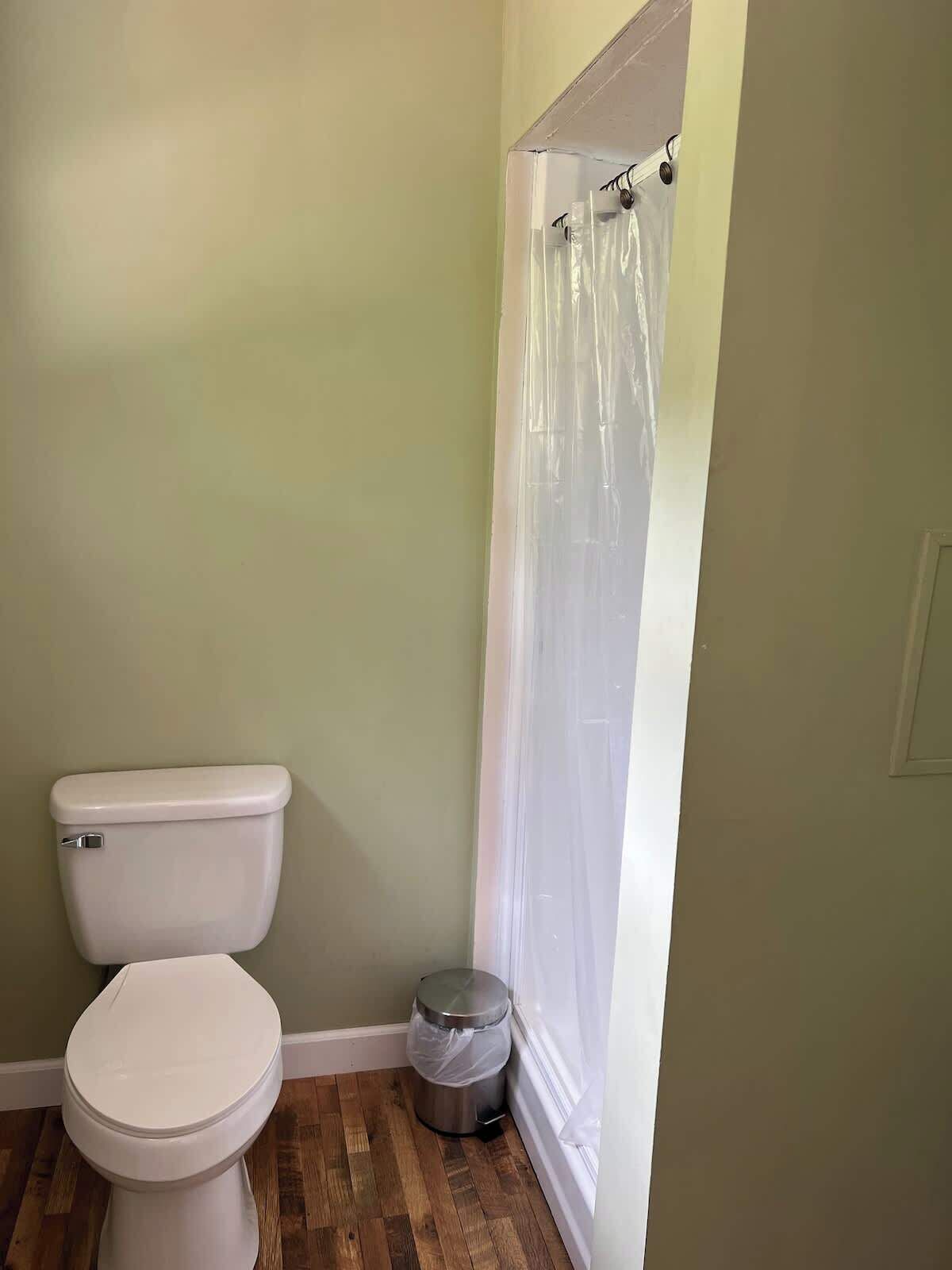 A small bathroom with a toilet, a trash can, and a shower curtain.