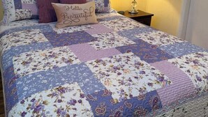 A bedroom with a floral quilted bedspread, a bedside lamp, and a pillow with the text "hello Beautiful". - The Barn at Wendover - 4 BR 2 BA (Wendover)