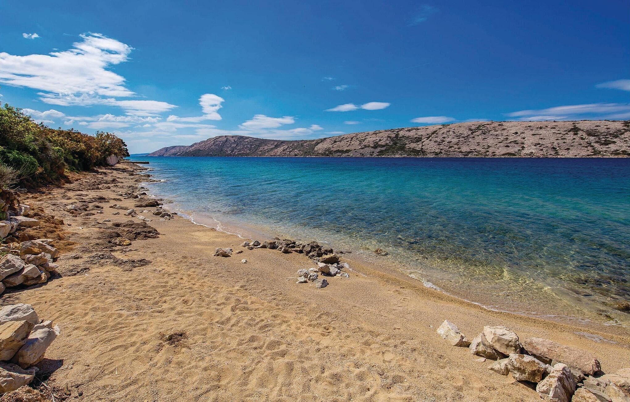 Une plage à l’eau d’un bleu limpide, avec un rivage rocheux et une montagne qui se profile à l’horizon.