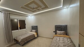 A modern bedroom with two beds, a ceiling light fixture, and a window with curtains. - Fantastic 3-bedroom apartment in cool Oujda for your stay (Oujda)