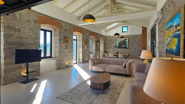 A spacious living room with a stone wall, a large sofa, a coffee table, and a TV mounted on the wall. - Nice home in Poljane with sauna (Poljane)